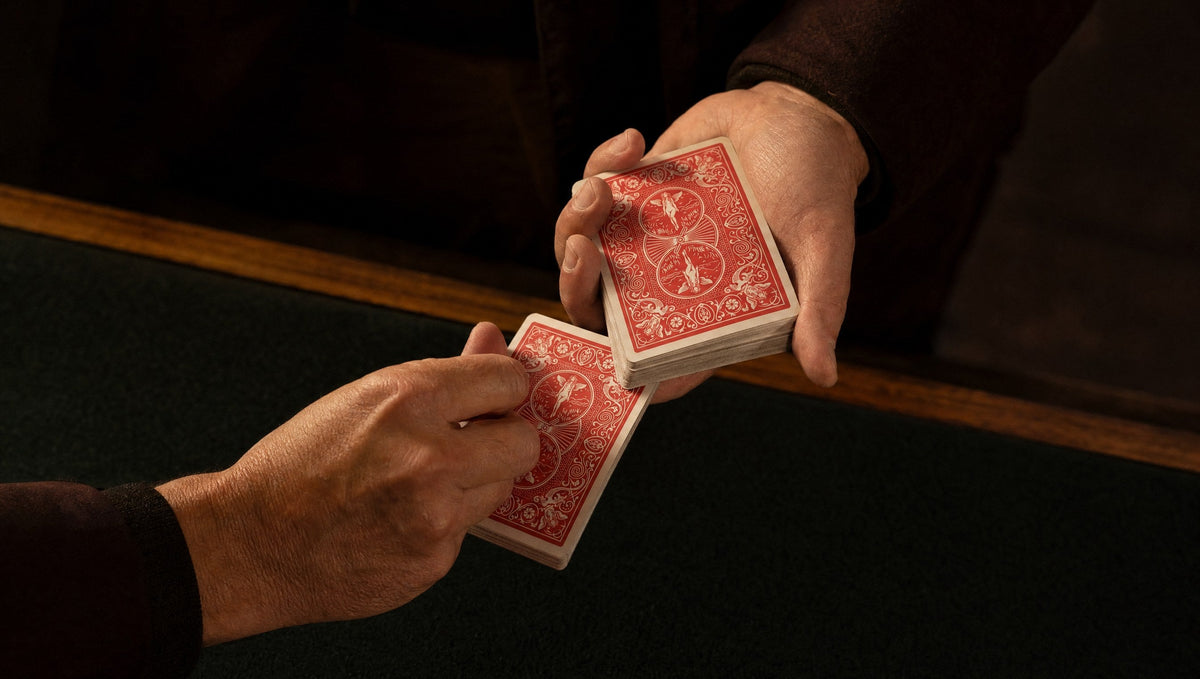 A magician’s hand holding a red-backed deck while a spectator’s hand takes a card