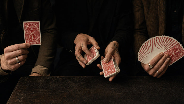 Three performers’ hands: one showing a single card, one cutting packets, one holding a fan of cards
