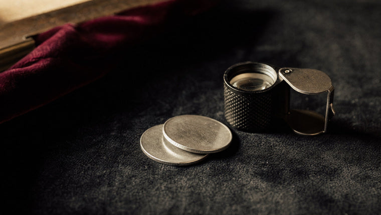 Two silver coins stacked on dark velvet beside a jeweller’s loupe