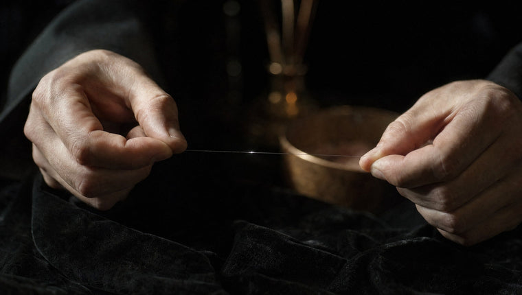 Two hands stretching a fine clear thread that catches the light over black velvet