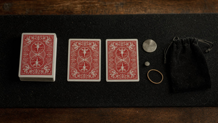 A deck, two red-backed cards, a plain silver disc, a magnet, a rubber band and a velvet pouch laid out on black felt