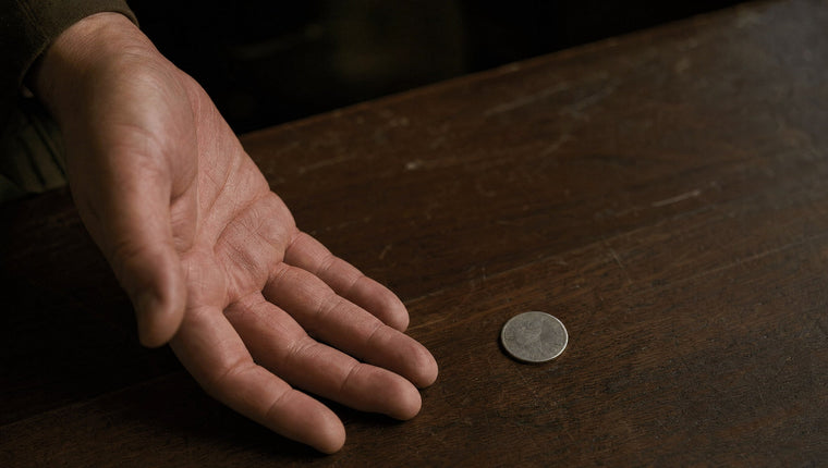 A relaxed open hand beside a worn silver coin on a walnut table