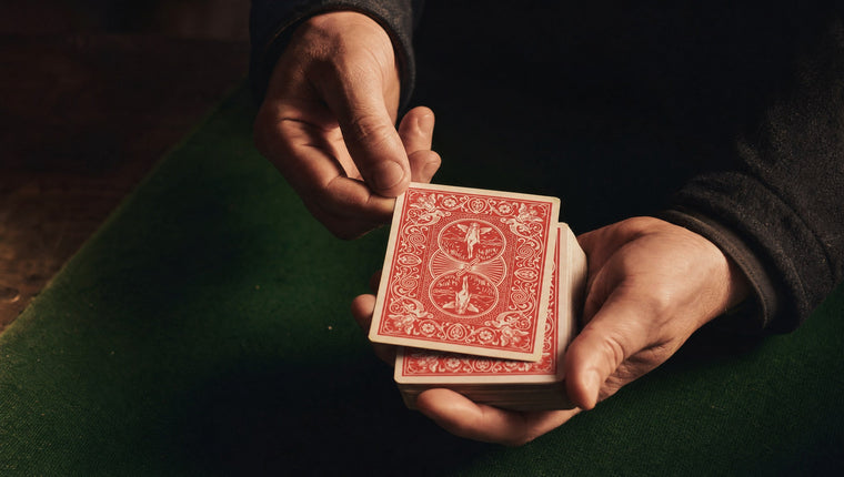 A hand lifting the top card of a face-down deck over a green close-up mat