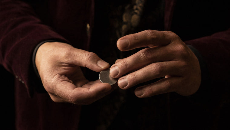 Two hands at the moment of a coin vanish, one reaching to take a silver coin from the other