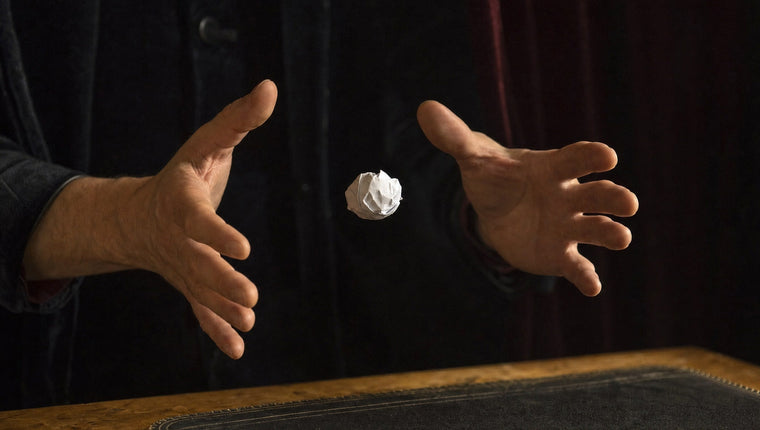 A small paper ball floating between two open hands against dark velvet