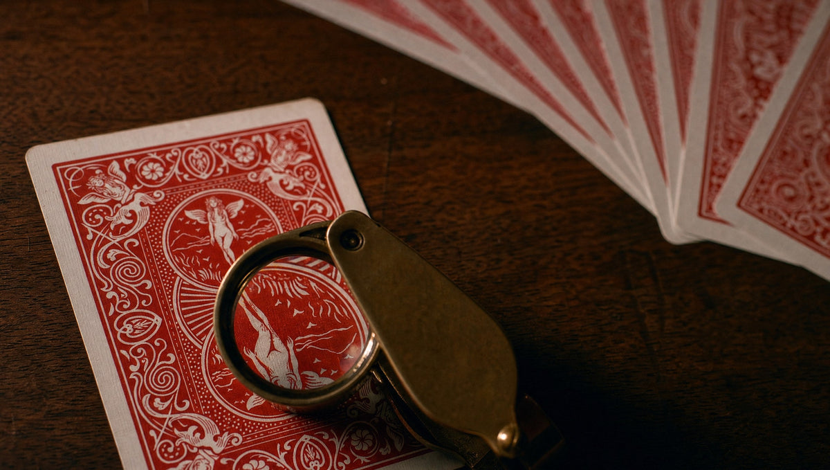 A jeweller’s loupe over the back of a red playing card on dark wood, a fan of cards behind
