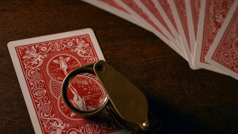 A jeweller’s loupe over the back of a red playing card on dark wood, a fan of cards behind