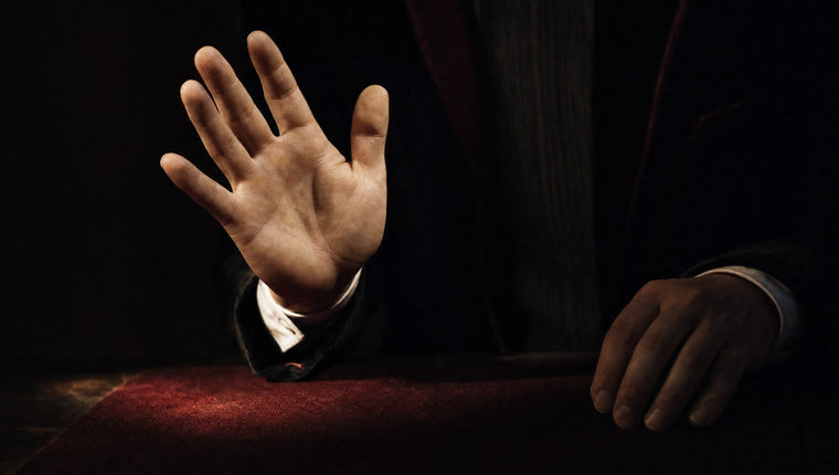 A magician’s raised open hand in a spotlight while the other hand rests in shadow
