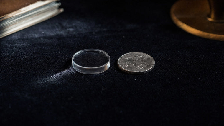 A clear acrylic disc beside an ordinary silver coin on black velvet