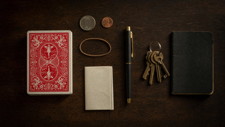 An everyday carry flat lay: a deck of cards, coins, a rubber band, a pen, keys and a notebook