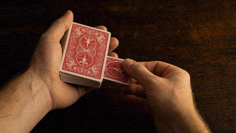 A hand drawing a single card out of the middle of a red-backed deck